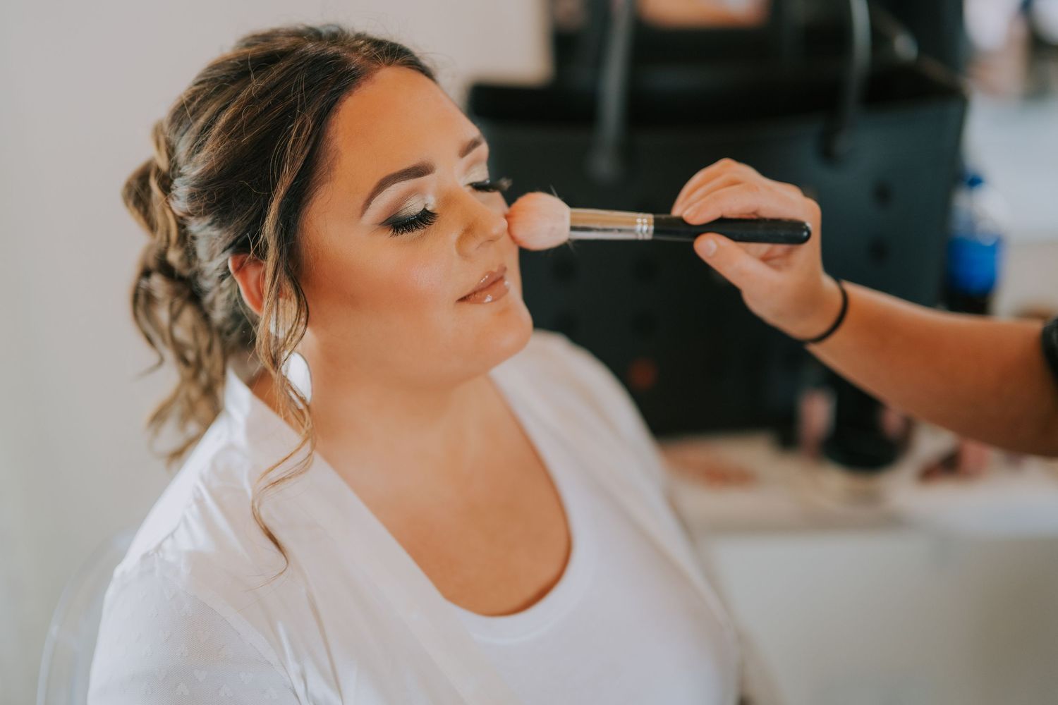 A makeup artist applies cosmetics to a bride during wedding day preparations.