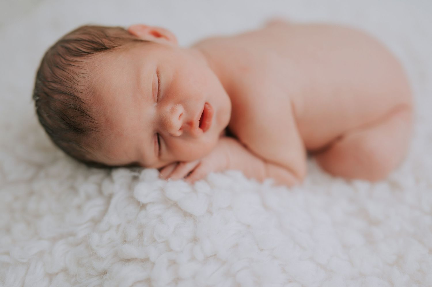 Sleeping newborn baby lying on soft white textured blanket in natural light.