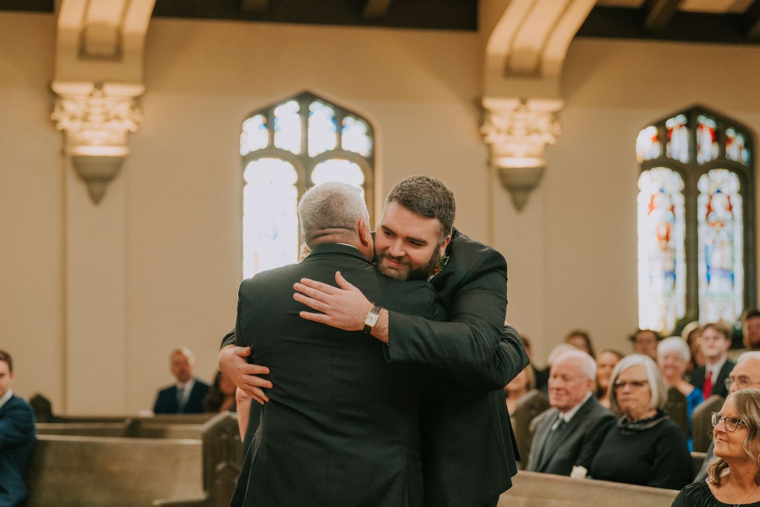 Two people embrace during an emotional moment at a church ceremony while guests look on.