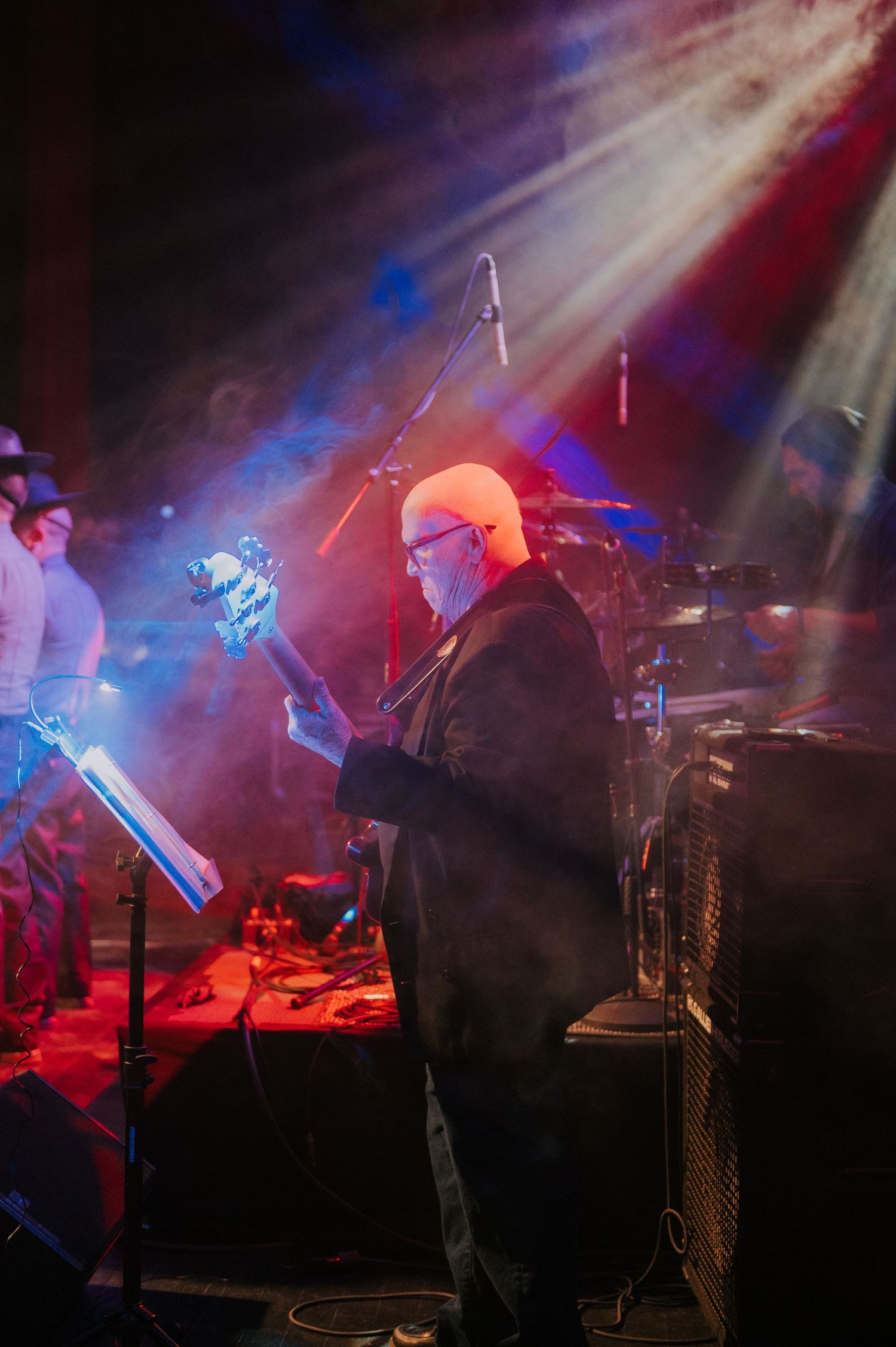 Musician performs on stage under dramatic lighting with blue and red spotlights creating an atmospheric effect.