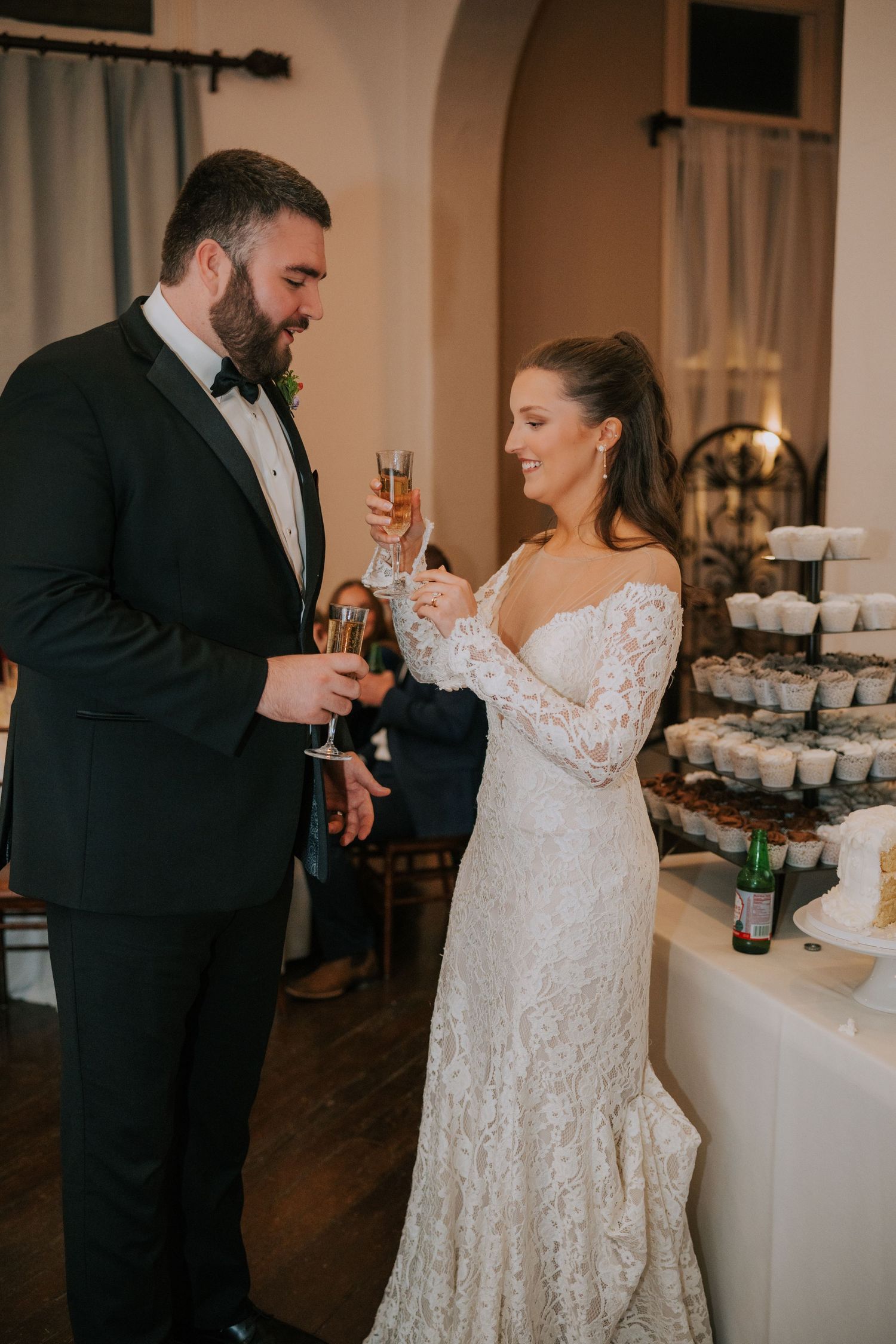 A couple shares a toast at their wedding reception beside an elegant tiered cupcake display.