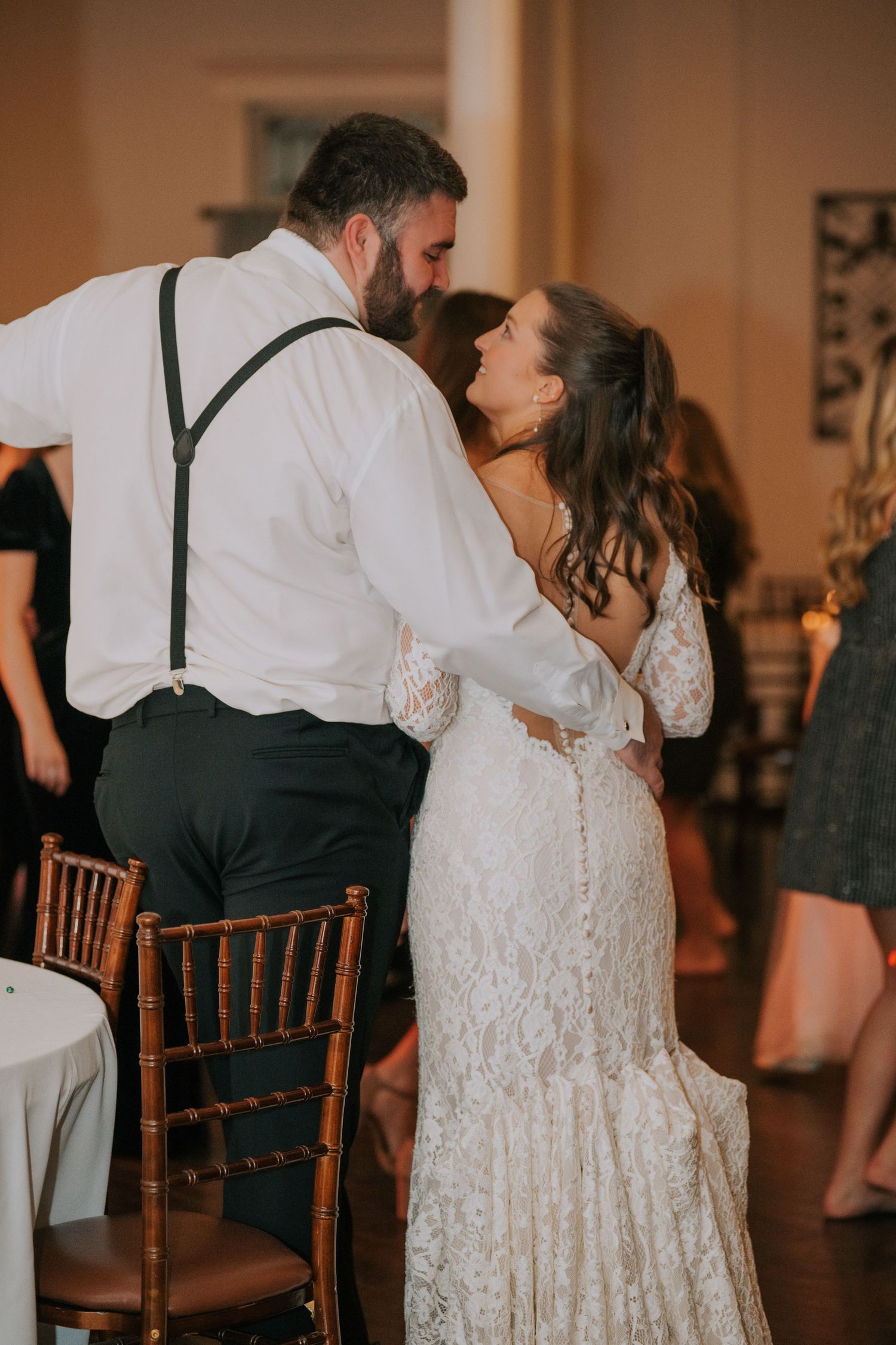 Newlyweds share an intimate dance moment at their wedding reception, bride wearing a beautiful lace gown with long sleeves.