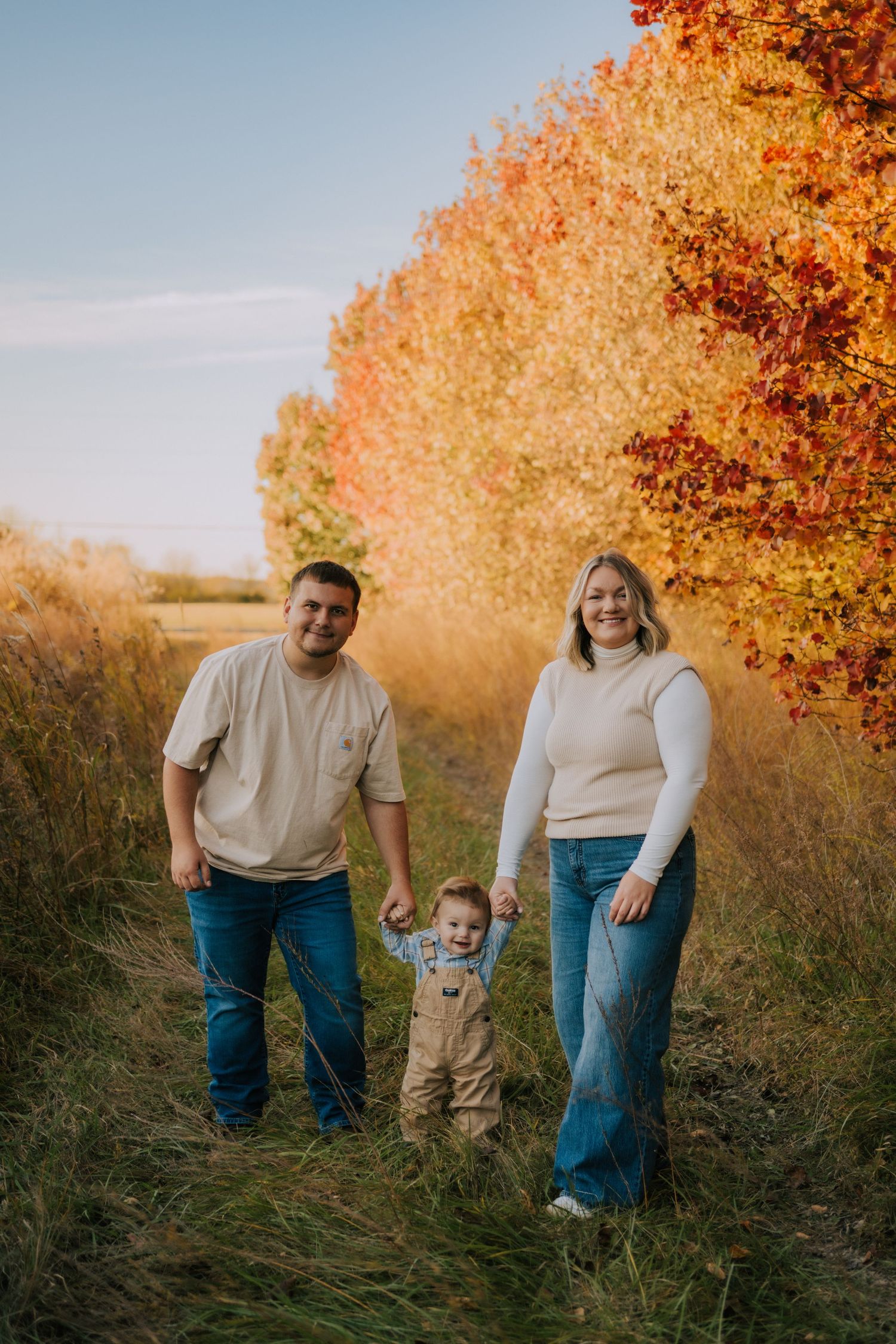 Family enjoying an autumn day together on a path lined with vibrant orange and red trees.