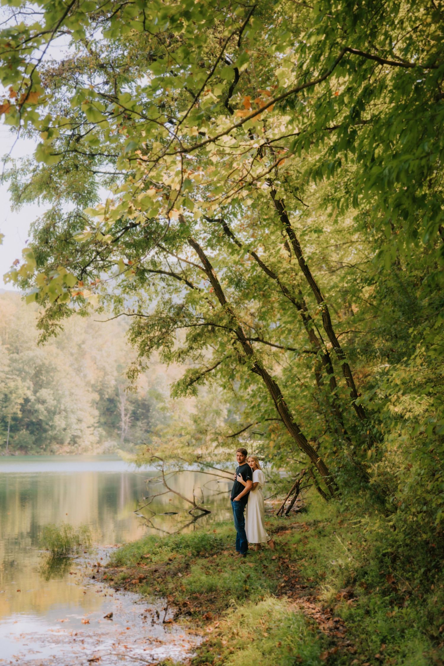 Romantic couple shares intimate moments in a secluded forest setting near a tranquil lake.