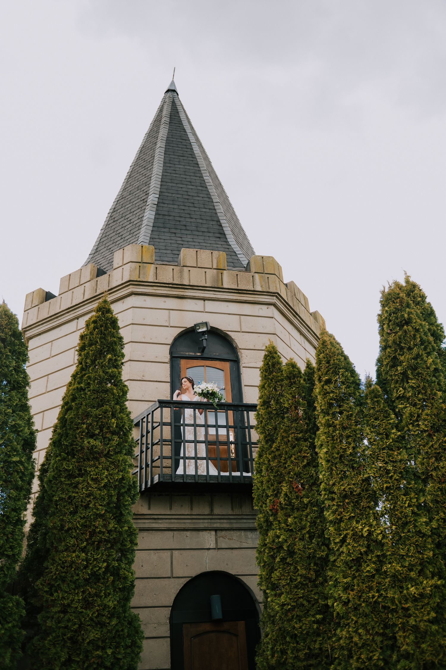 Gothic stone castle tower with pointed spires and evergreen trees in foreground.