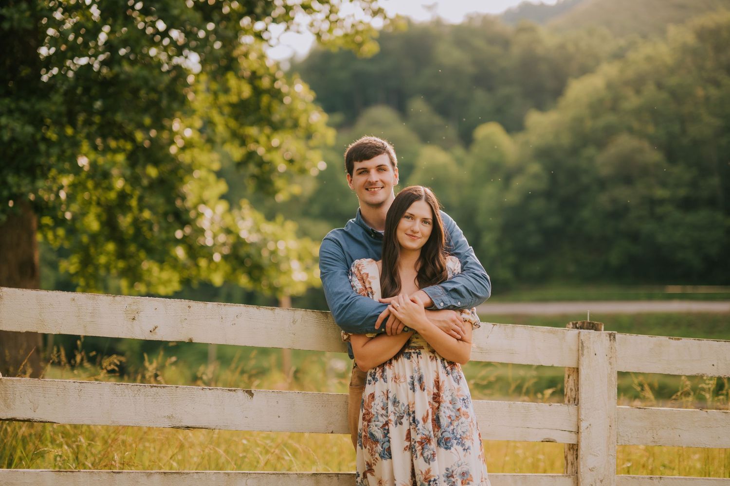 A romantic couple embraces in a golden sunset field with mountains in the background.