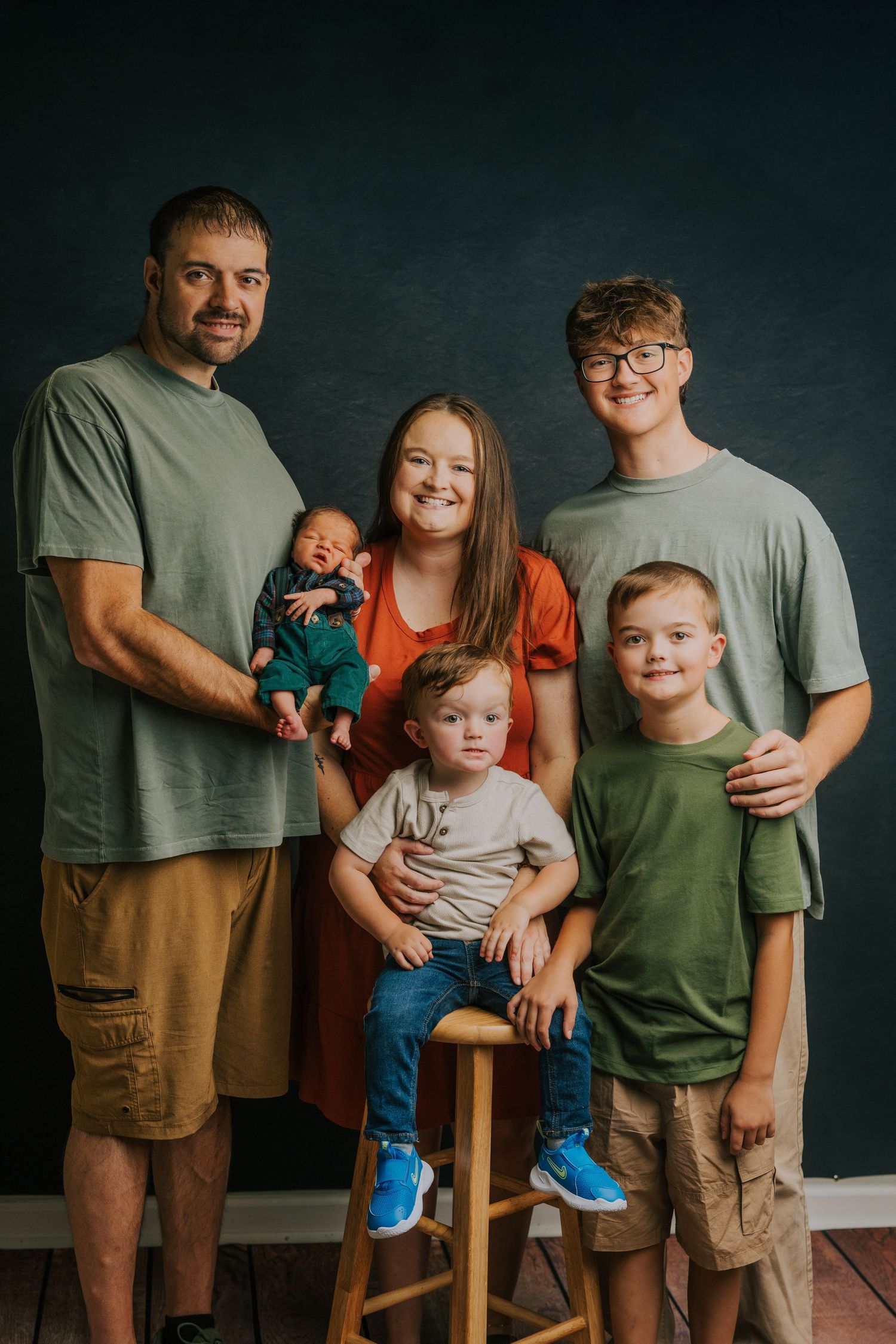 Family portrait against dark background with casual outfits and natural poses.