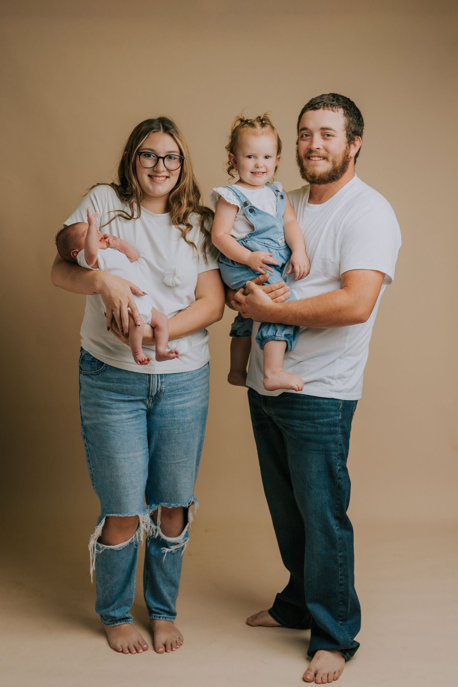 Casual family portrait session with denim and white t-shirts against beige backdrop.