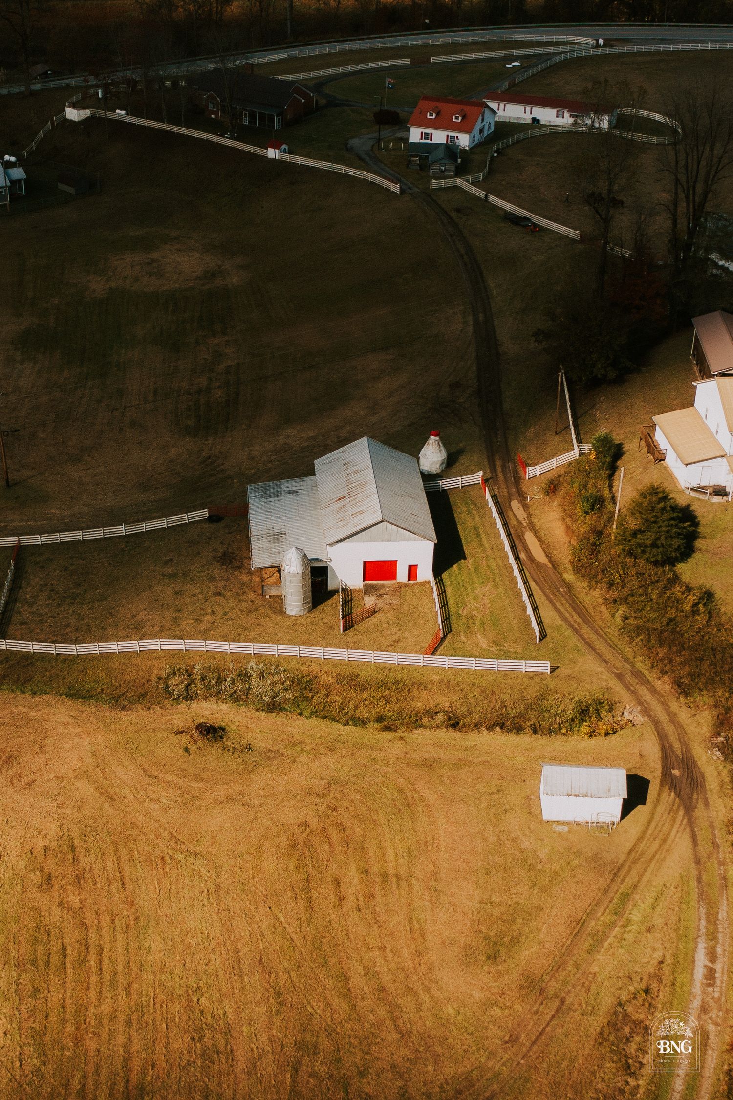 Aerial view of a rural farm property with red and white buildings connected by winding dirt paths.