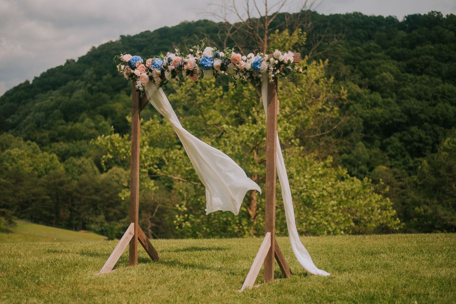 Rustic teepee structures set up in a scenic mountain field for outdoor wedding celebration.