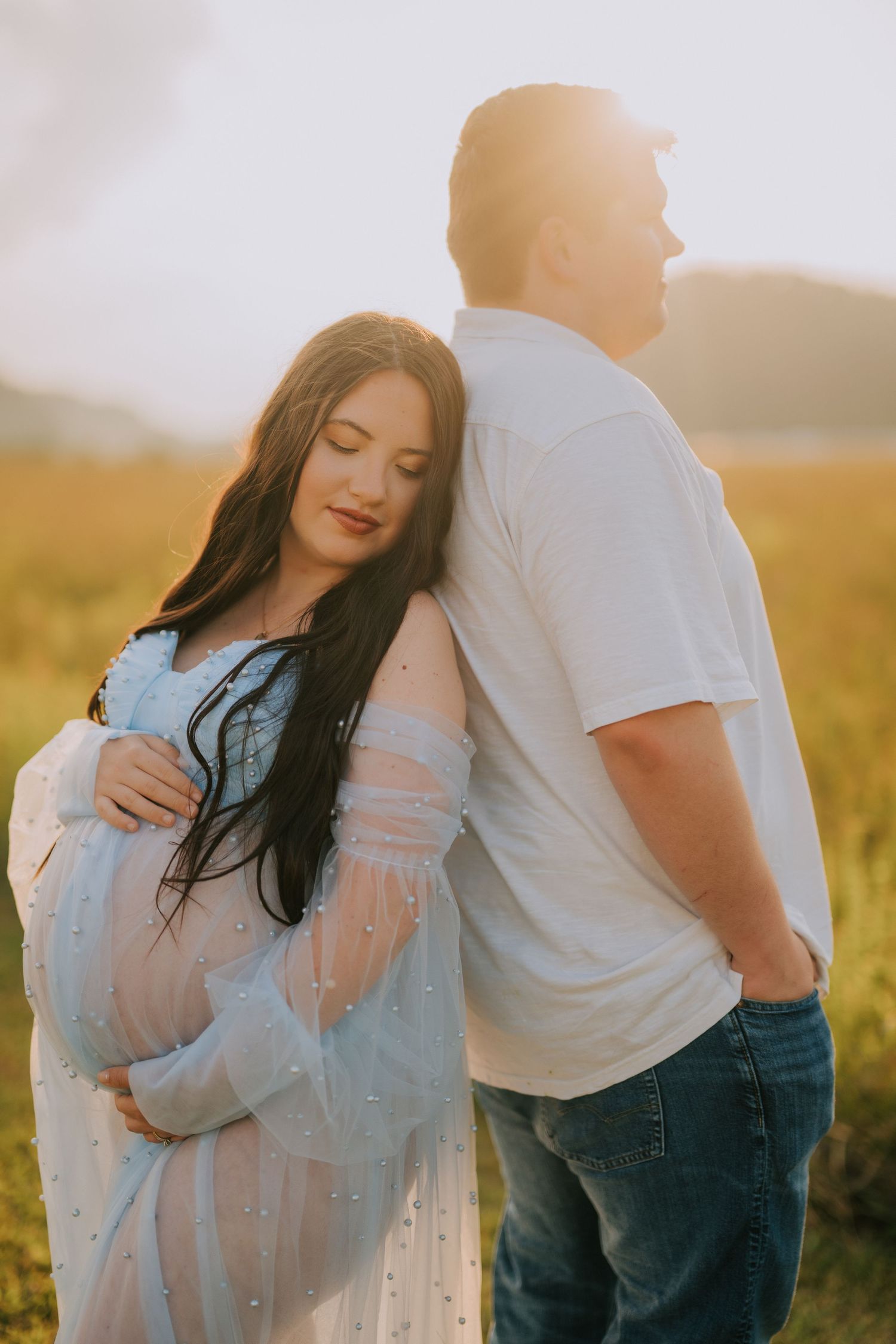 Intimate maternity portraits of couple embracing in a golden field at sunset.