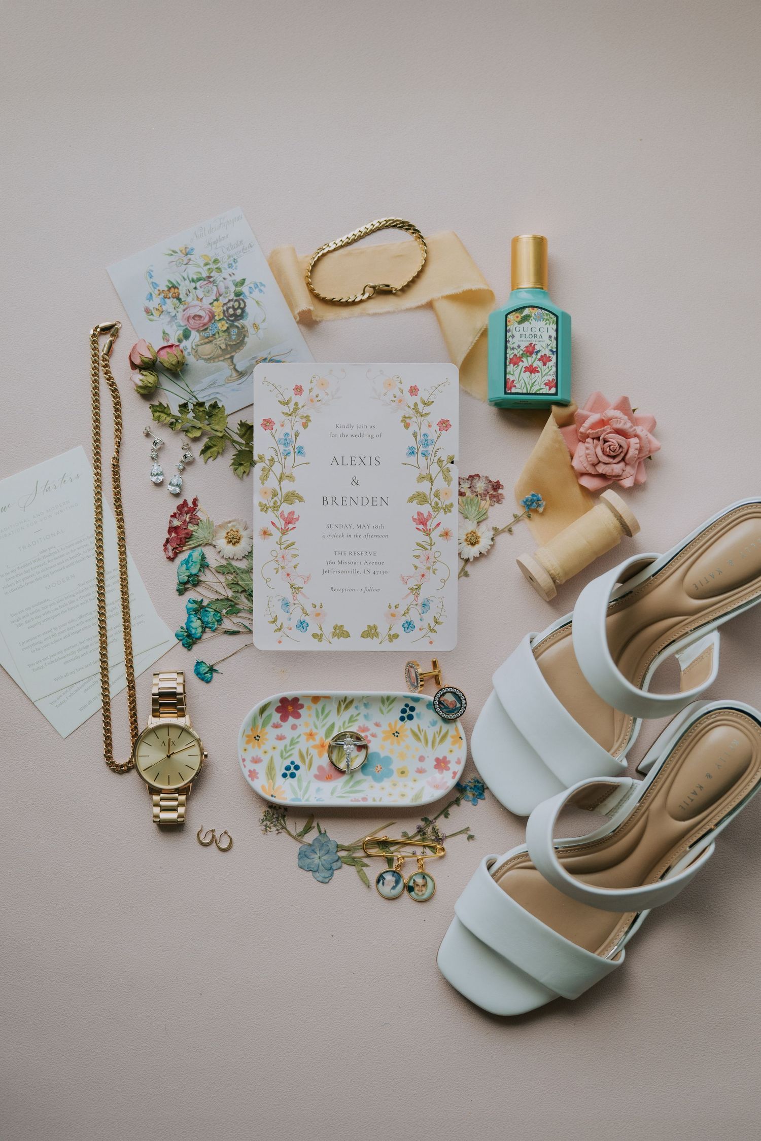 Wedding invitation suite with floral design, mint shoes and gold jewelry on white background.