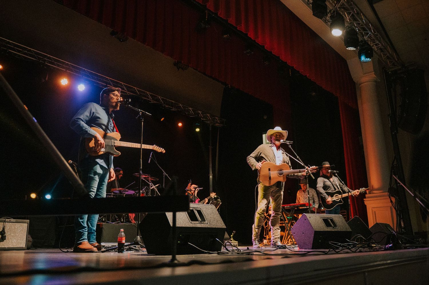 Folk band performing on a theater stage with traditional instruments and microphones.