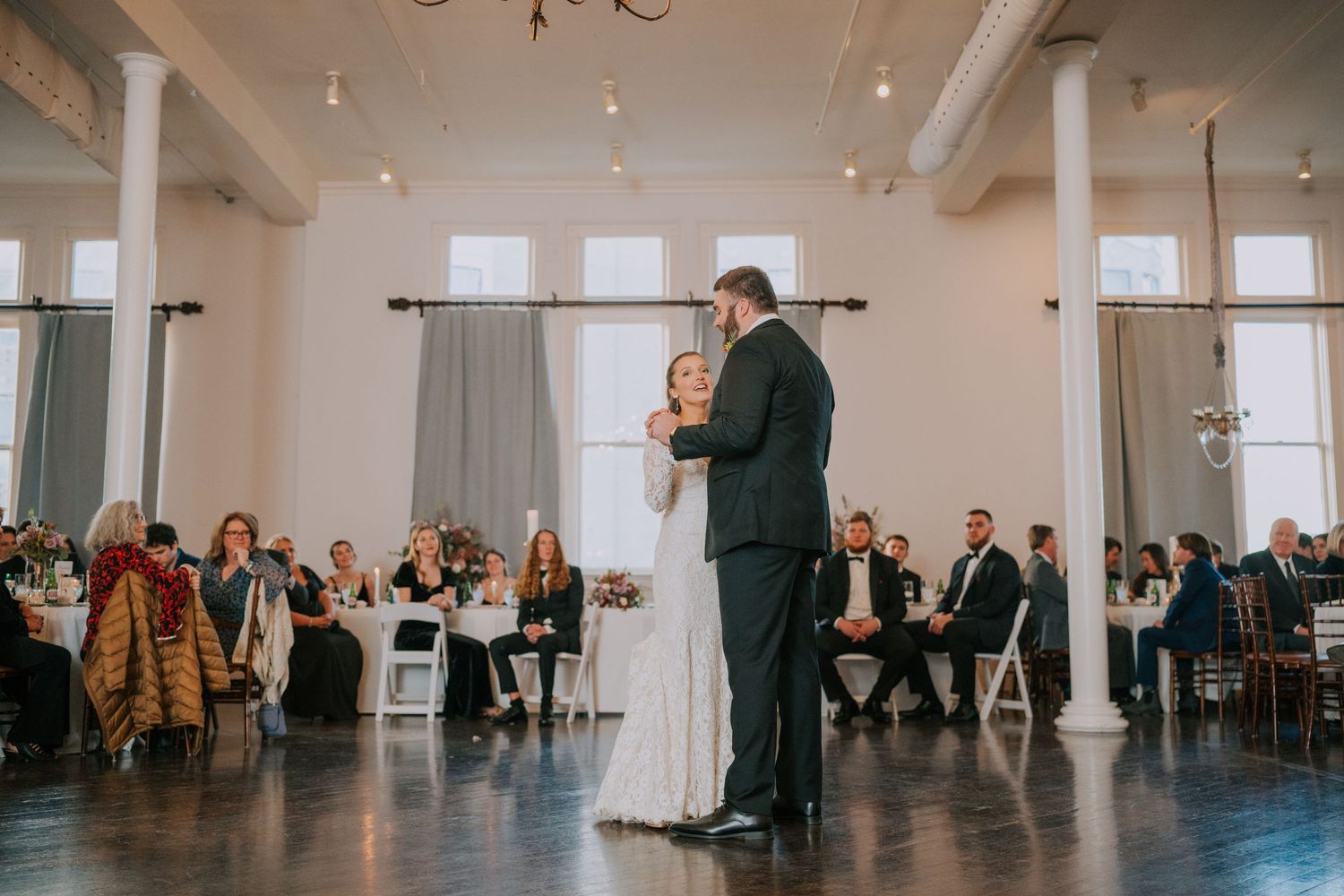 Couple dancing in an elegant venue while guests watch from their seats around the perimeter.
