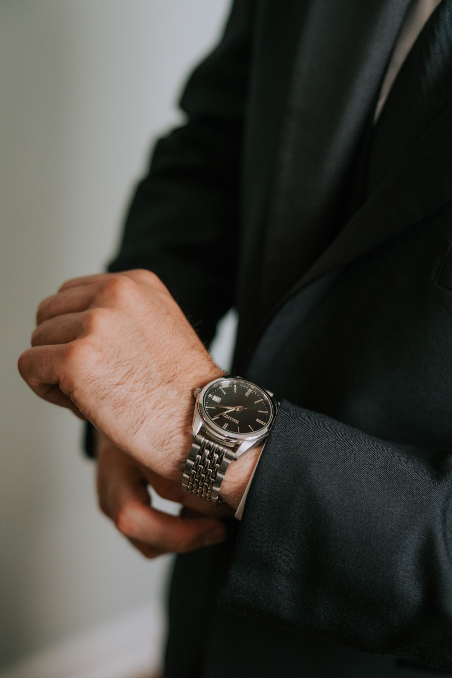 Close-up of a silver watch on a man's wrist with black suit sleeve.