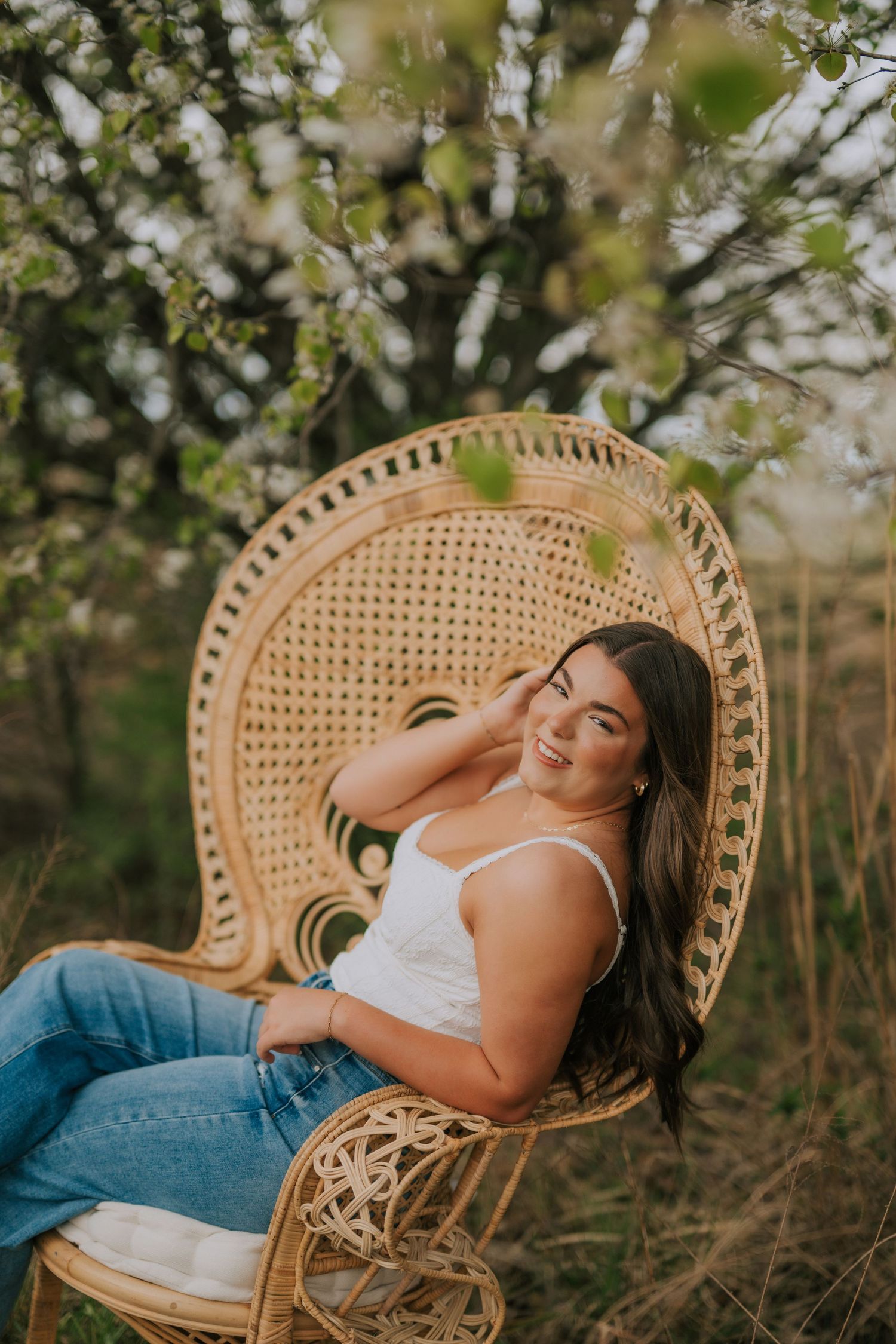 Outdoor portrait session in wicker peacock chair surrounded by spring blossoms.