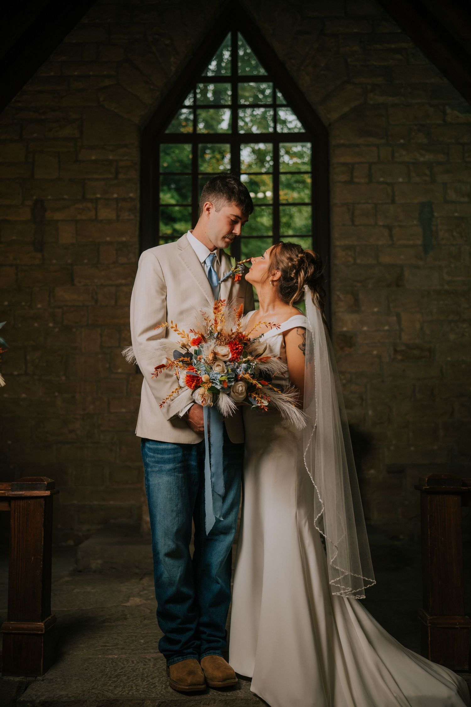 Romantic wedding couple embraces in a rustic stone chapel with natural light streaming through gothic windows.