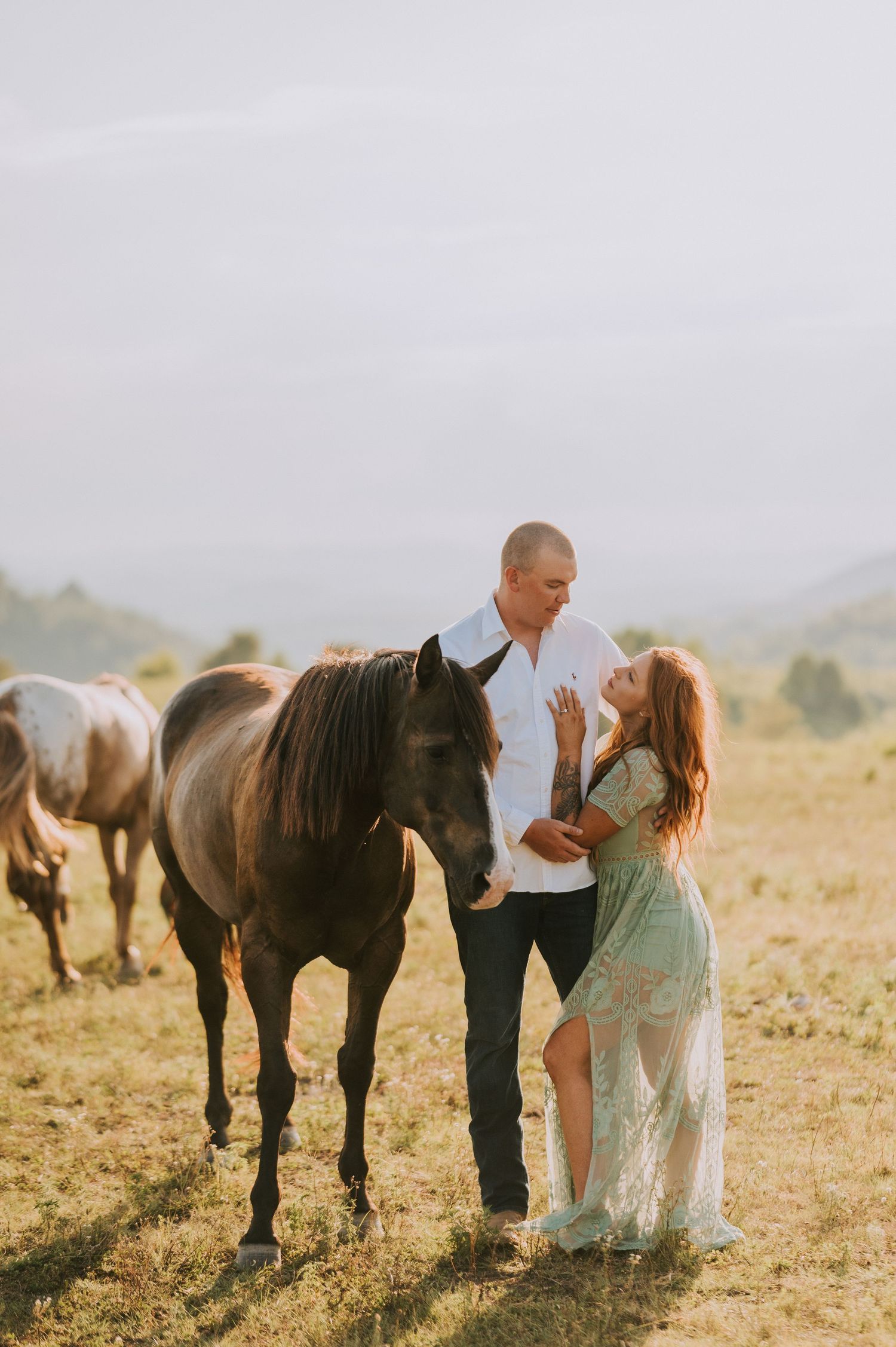 A couple interacts with horses in a scenic mountain field during golden hour.