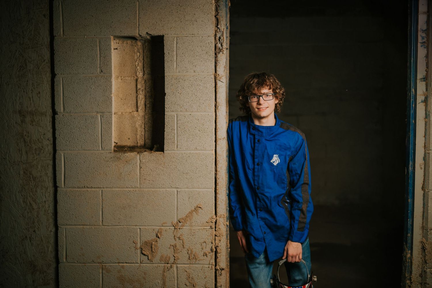 Figure in blue uniform stands against concrete block wall in dim lighting.