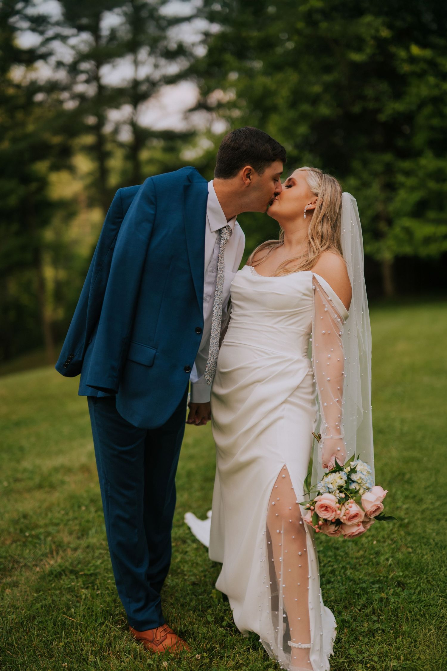 A romantic wedding couple embraces on a grassy lawn during their outdoor photo session.