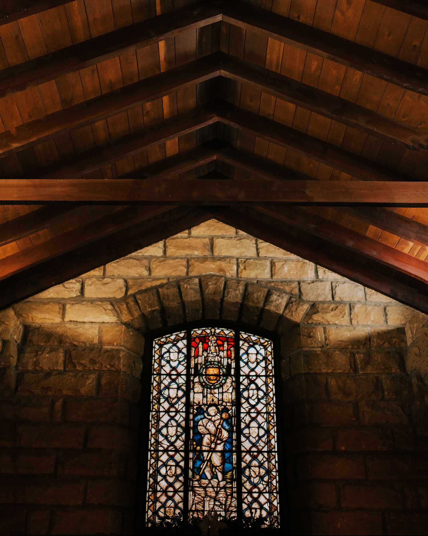 Series of stained glass windows in an old stone church with wooden beam ceiling.