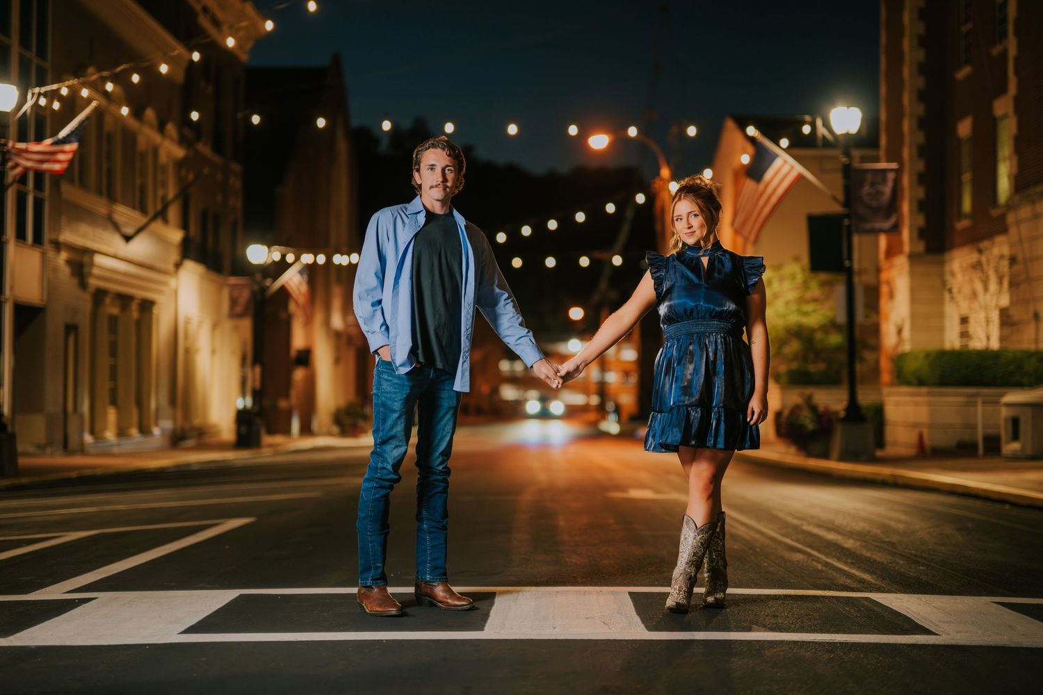 Couple walking together on a romantic nighttime city street illuminated by string lights.