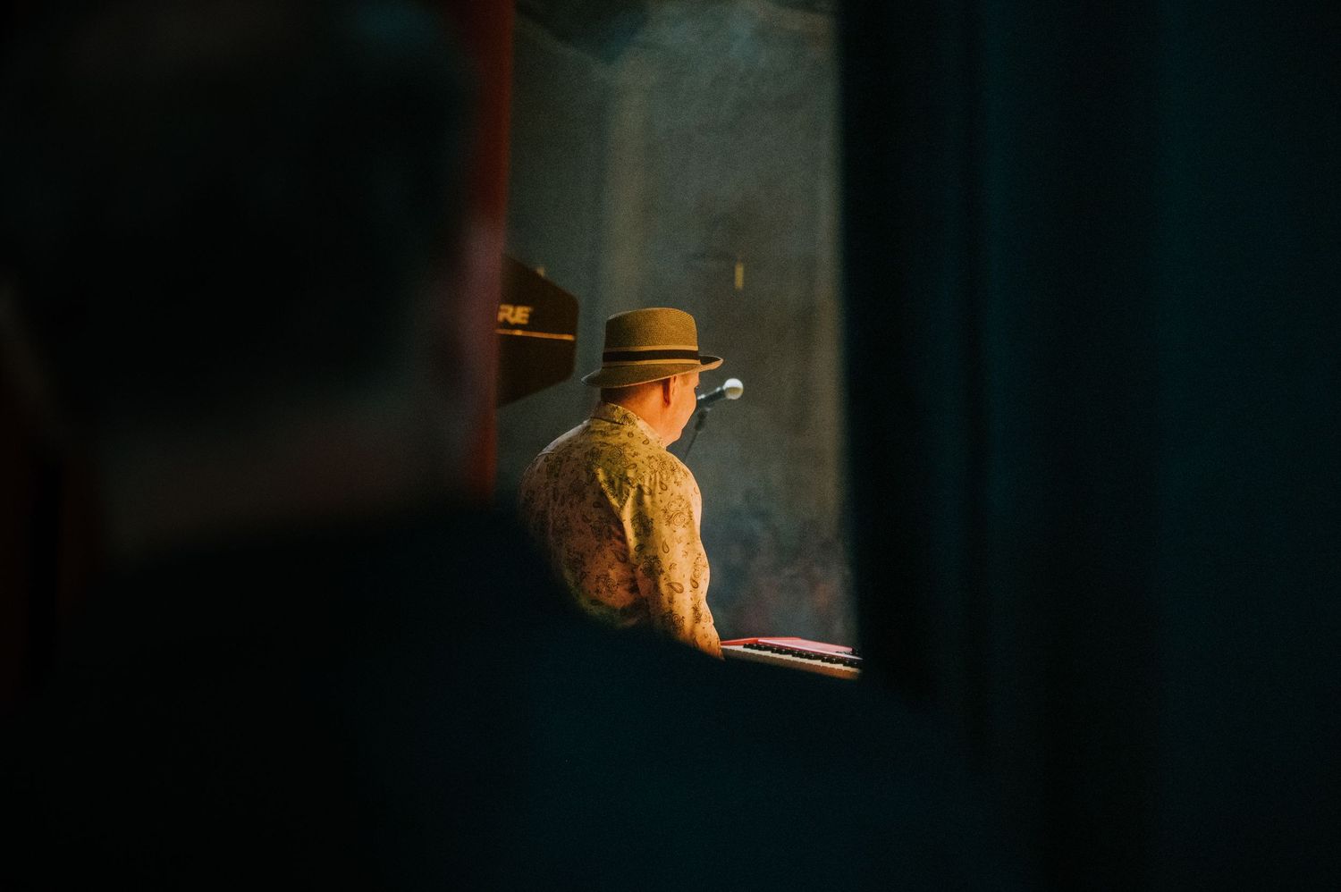 A person wearing a hat seen through a window in dramatic evening light, creating a moody silhouette.