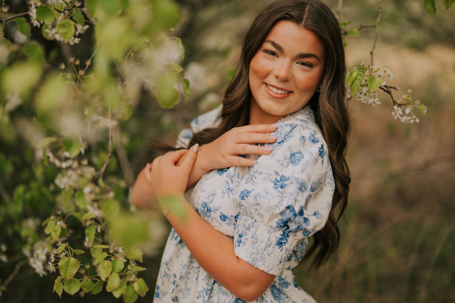 Spring portrait session in white floral dress among blooming trees and greenery.