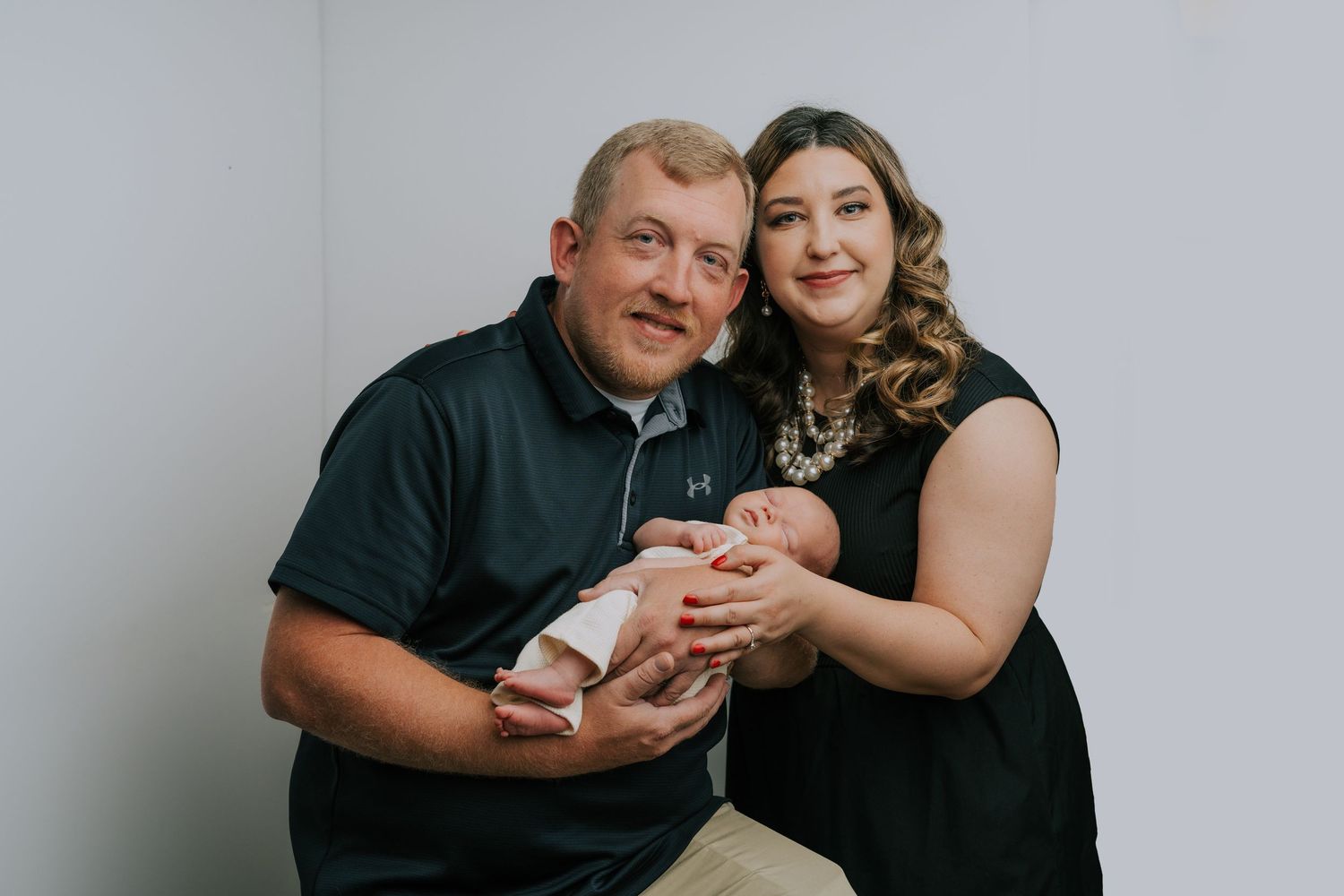 A family portrait with a newborn baby in a minimalist studio setting.