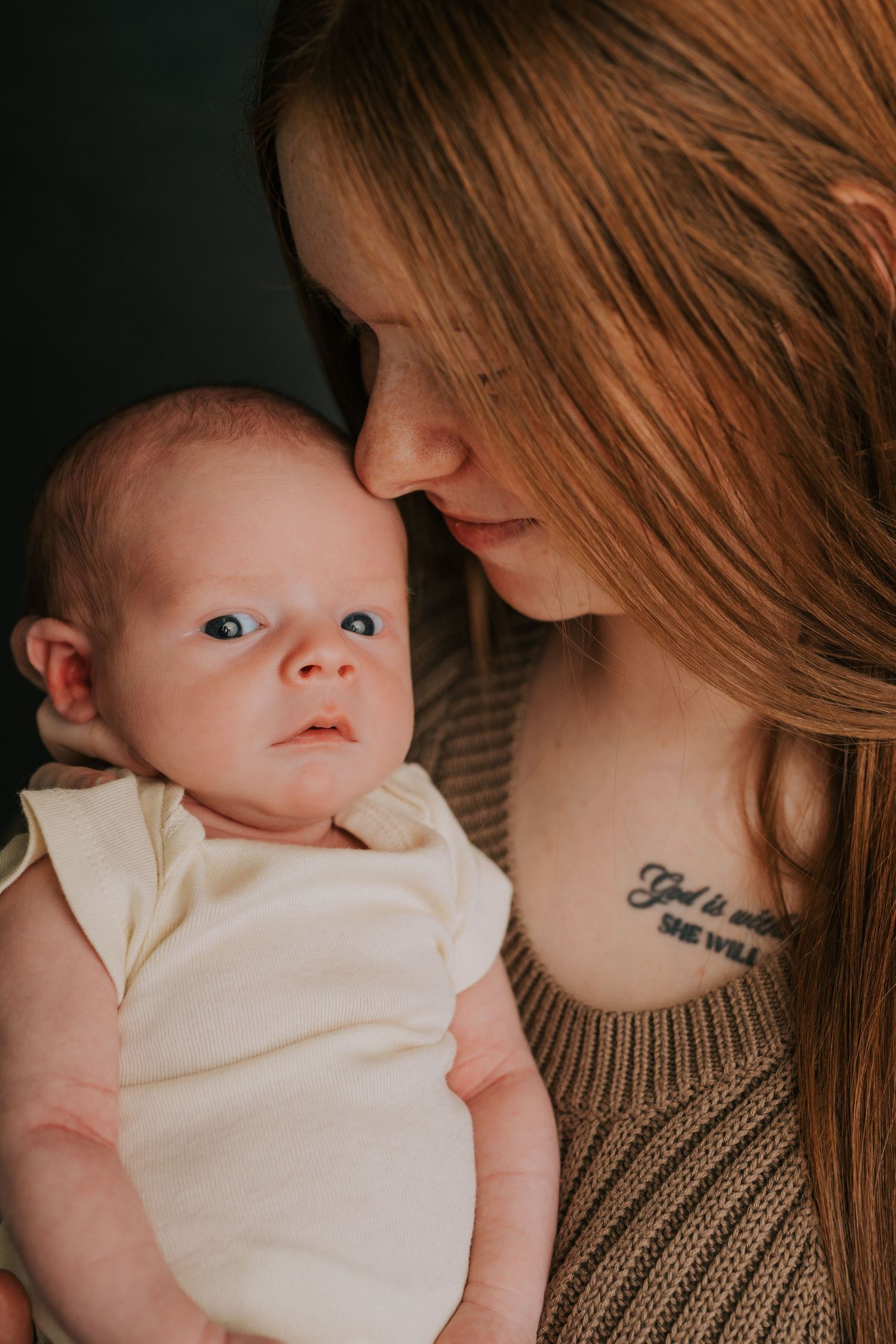 A baby in white clothing rests peacefully against a person wearing a brown sweater.