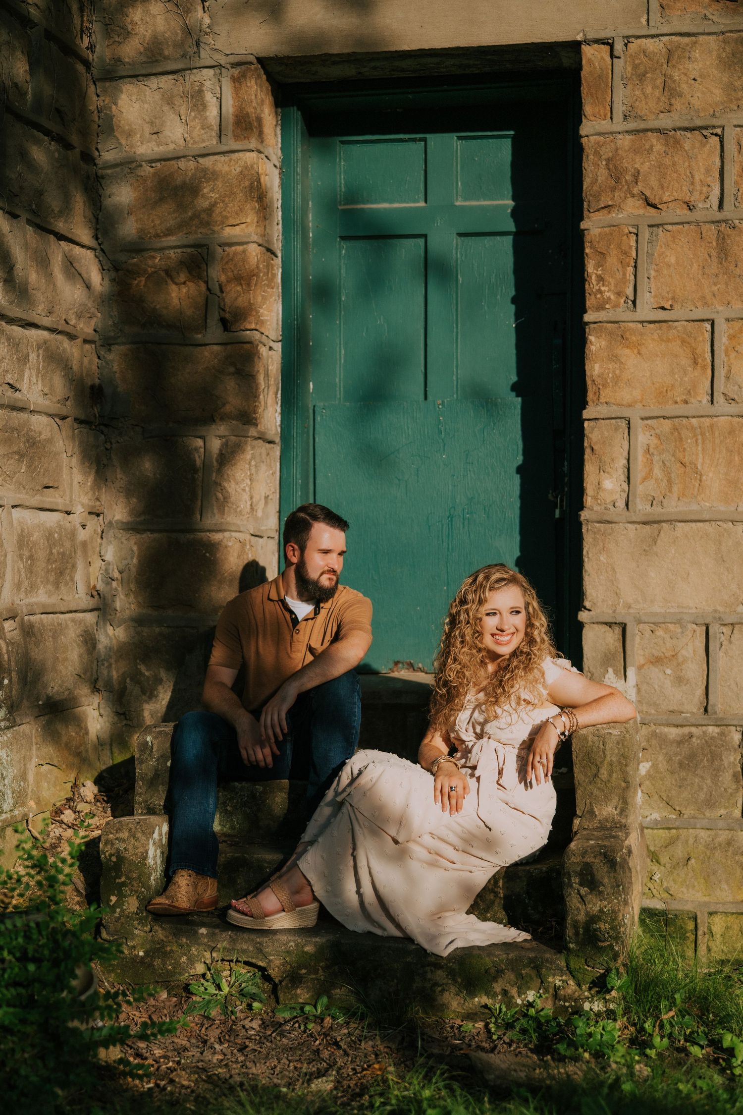 Couple poses against rustic stone wall with teal door in romantic photoshoot.