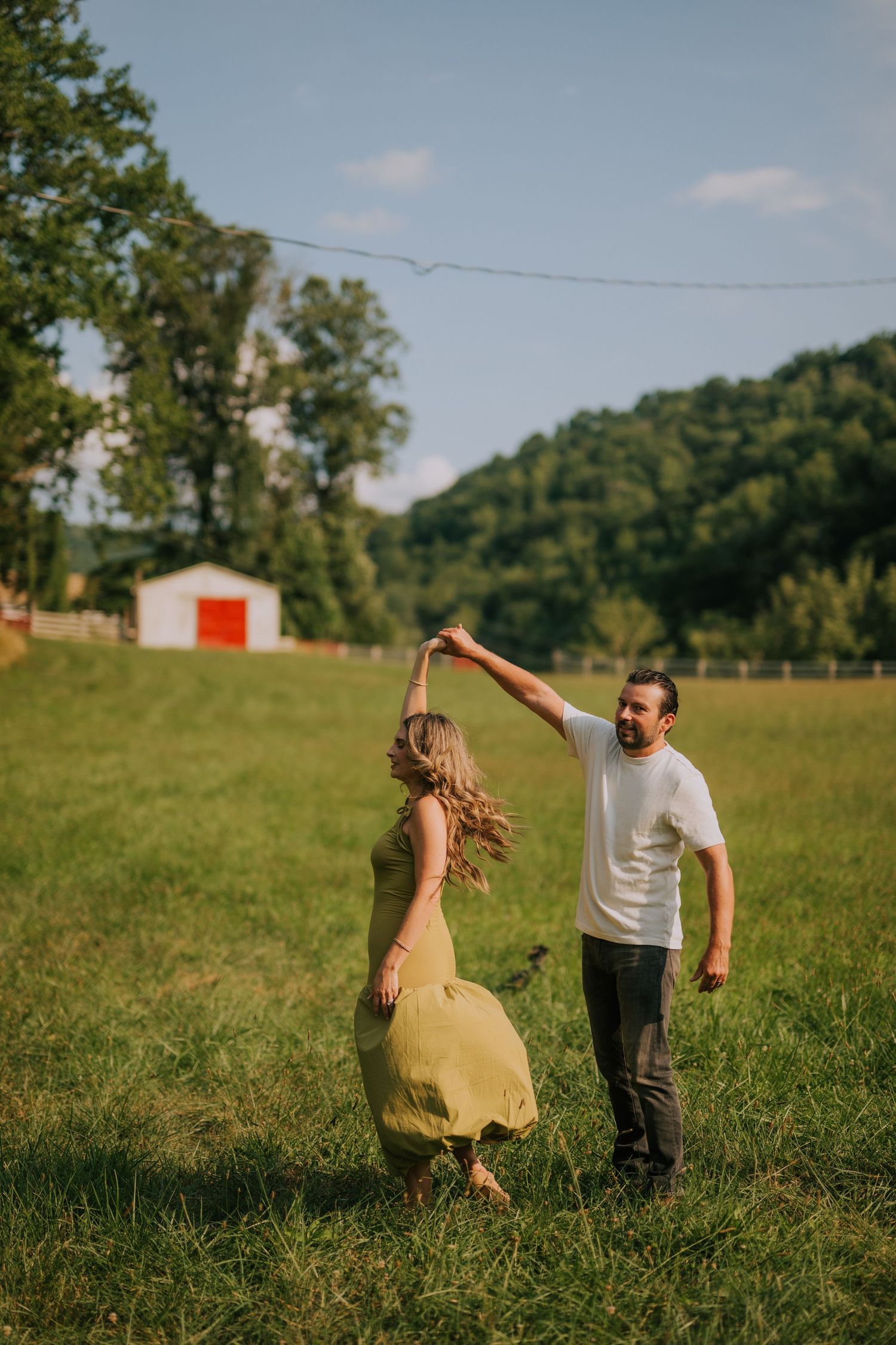 Playful couple dancing together in a sunny meadow with mountains in the background.
