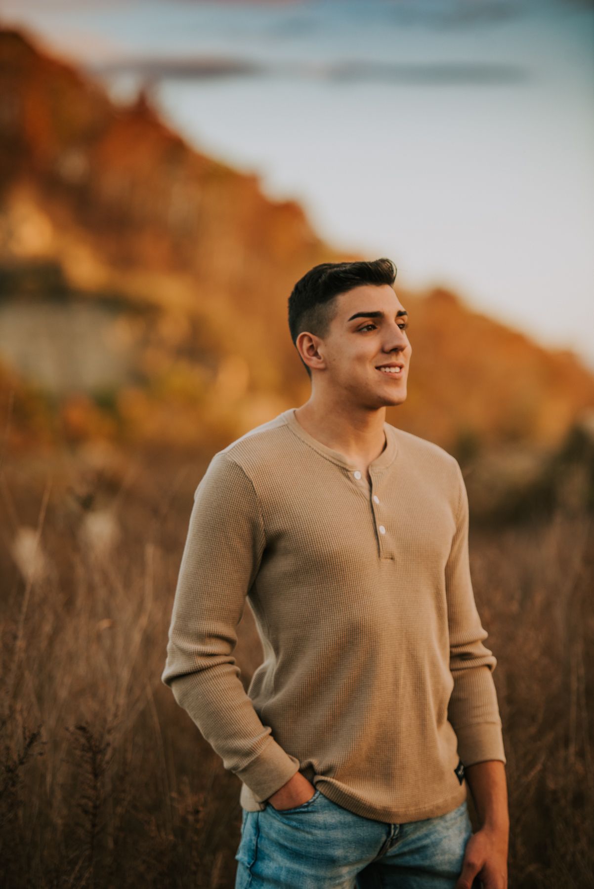 A person in a beige sweater poses against an autumn sunset backdrop.