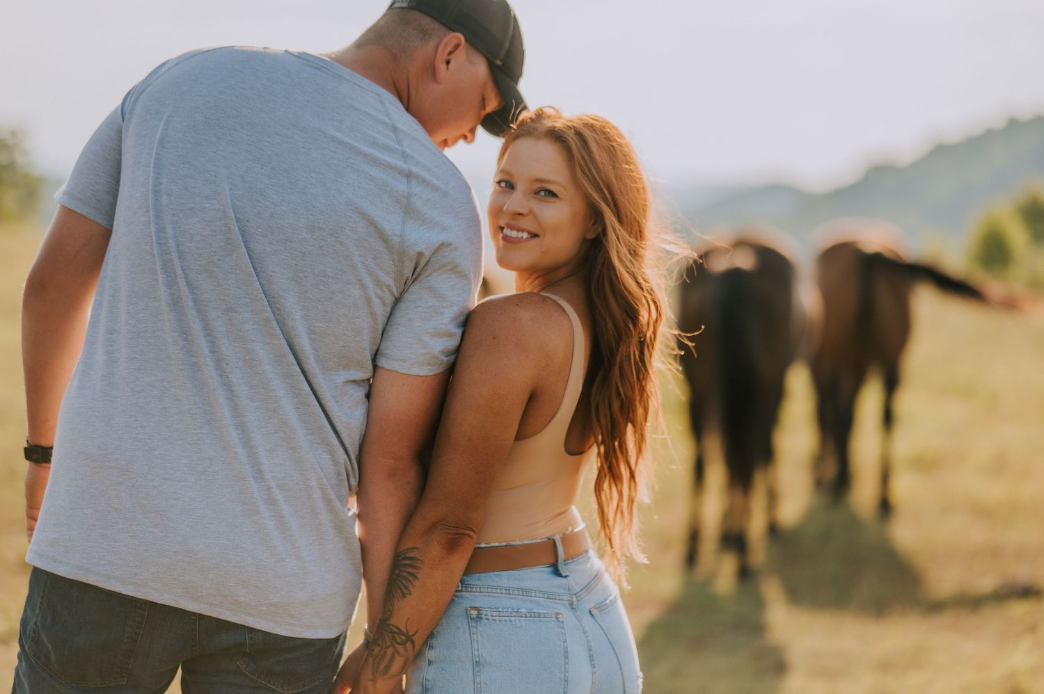 A couple shares tender moments at sunset with horses grazing in the background.