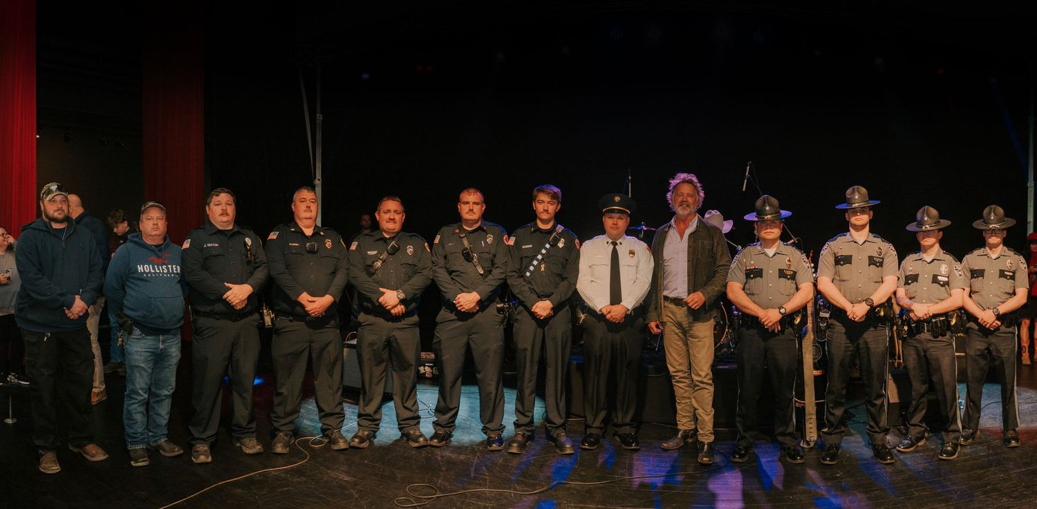 A line of uniformed law enforcement and public safety officers standing together on a dark stage for a group photo.