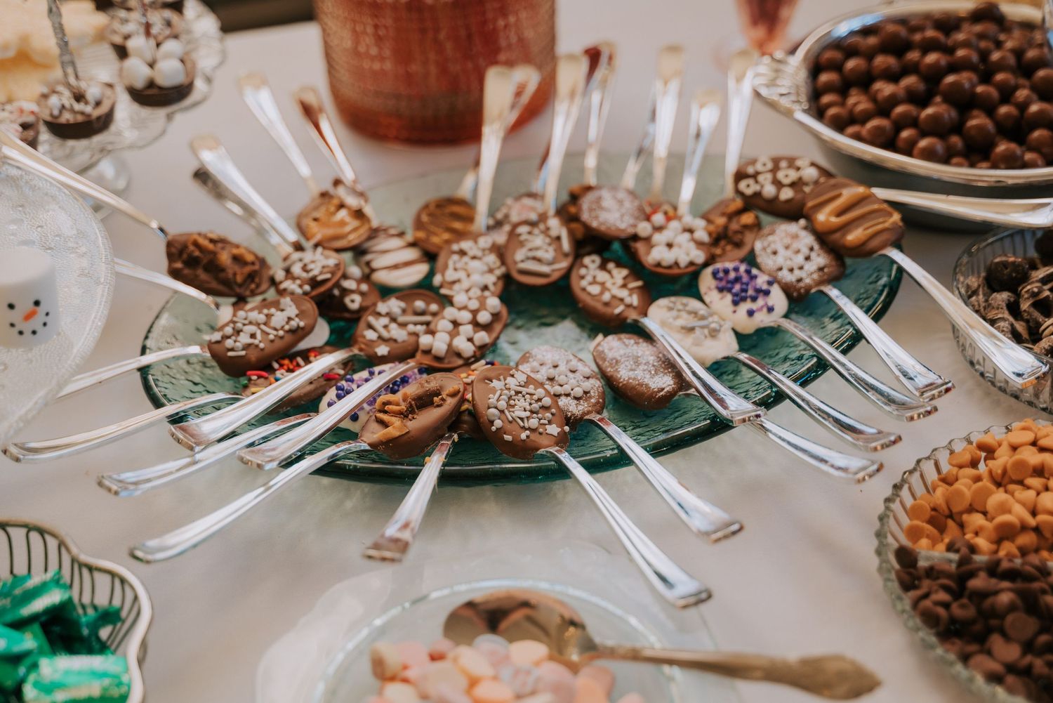 Chocolate-covered dessert spoons arranged in a circular pattern on a green plate at a holiday party setting.