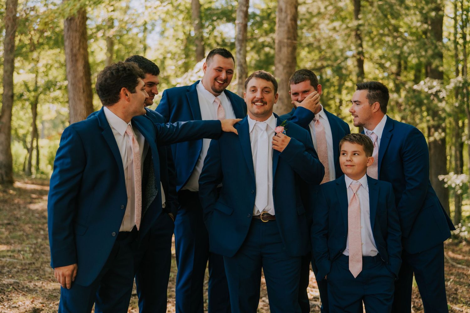 Groomsmen in navy suits stand together outdoors for wedding party photo.