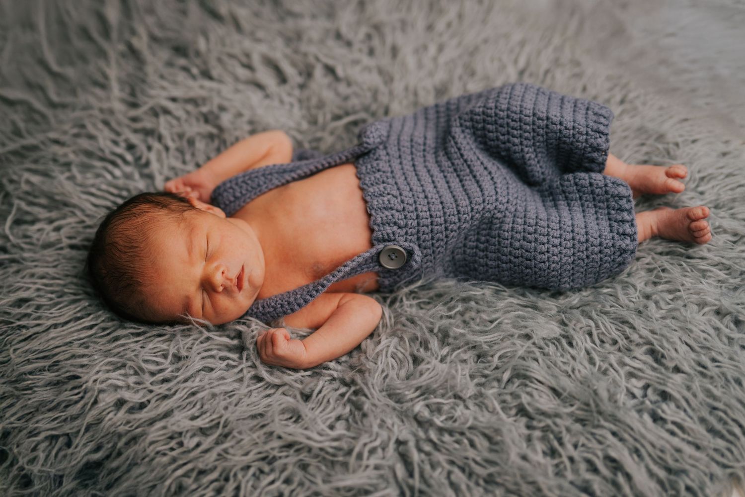 Peaceful newborn sleeping on soft gray textured blanket during professional photo session.