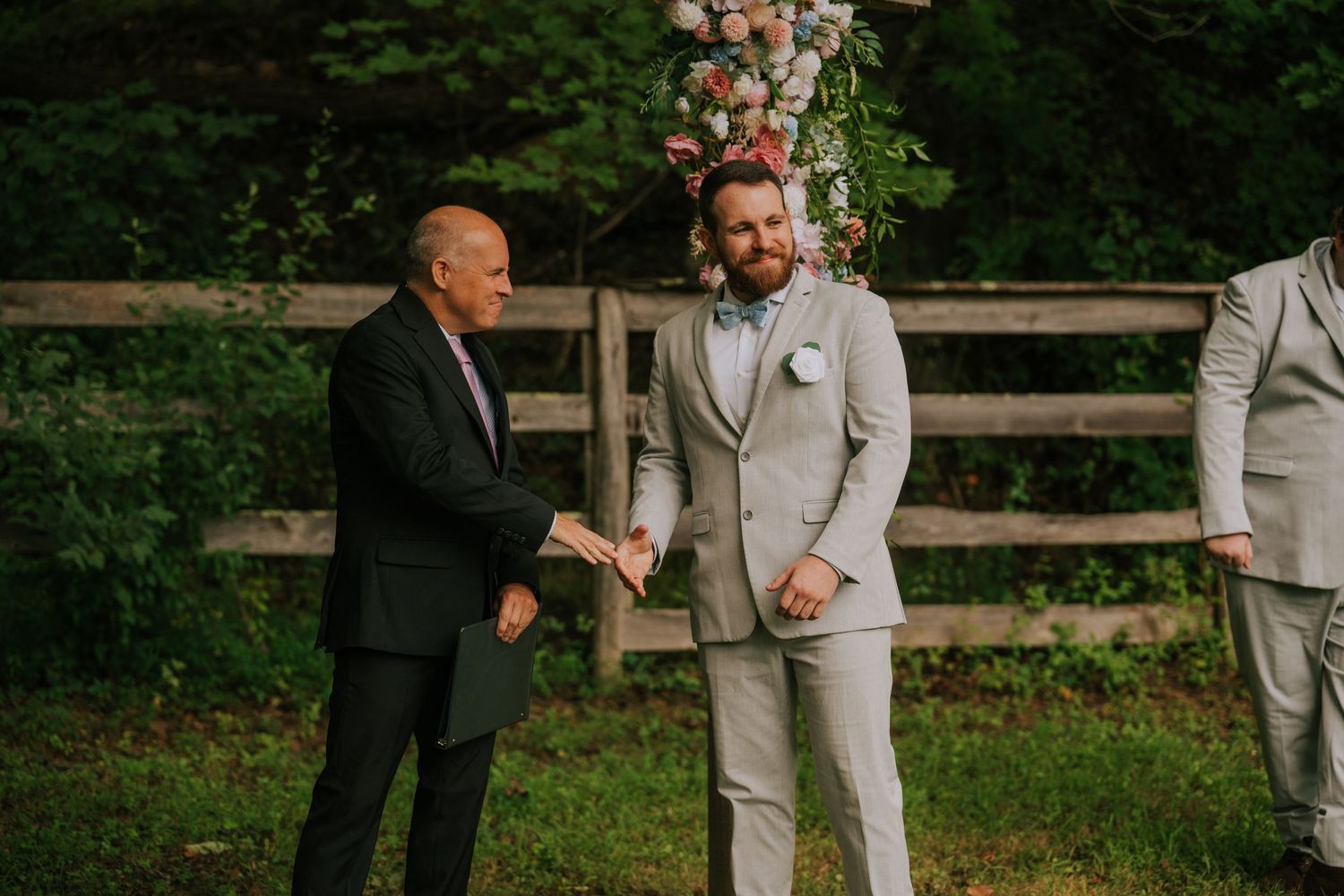 Wedding party members in formal attire gather for photos against a natural outdoor setting.
