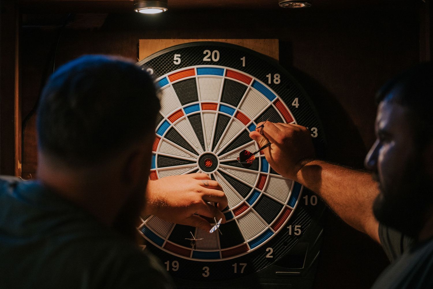 Three people playing darts in a dimly lit room.