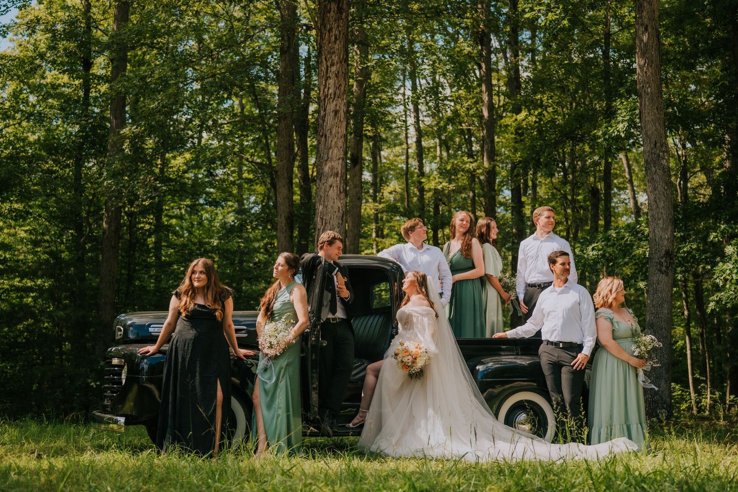 Wedding party poses together in a lush green forest setting during golden hour.