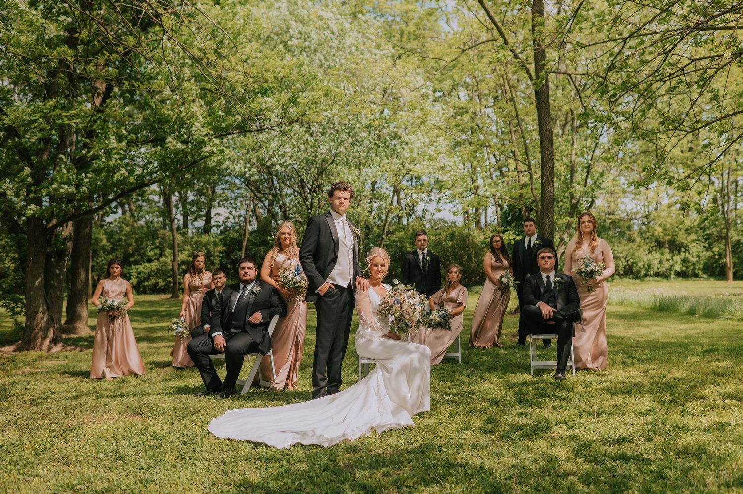 Wedding celebration in sunlit garden with flowing dresses and natural greenery.