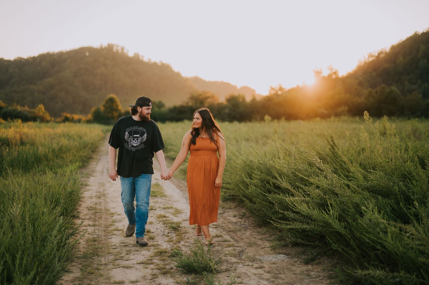 Couple walking down a country path at golden hour surrounded by tall grass.