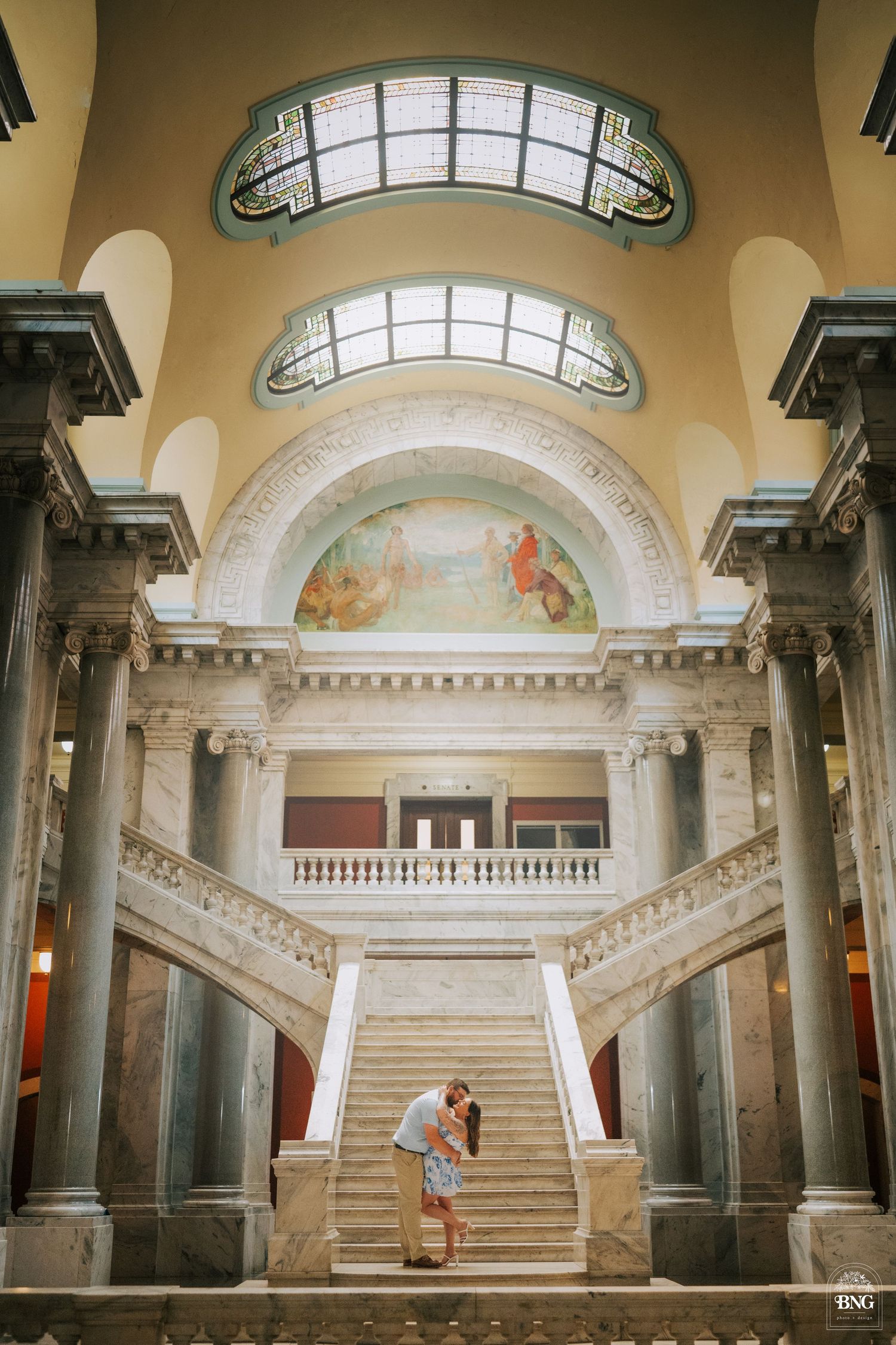 Wide angle view of a classical marble interior with grand staircase and arched windows.