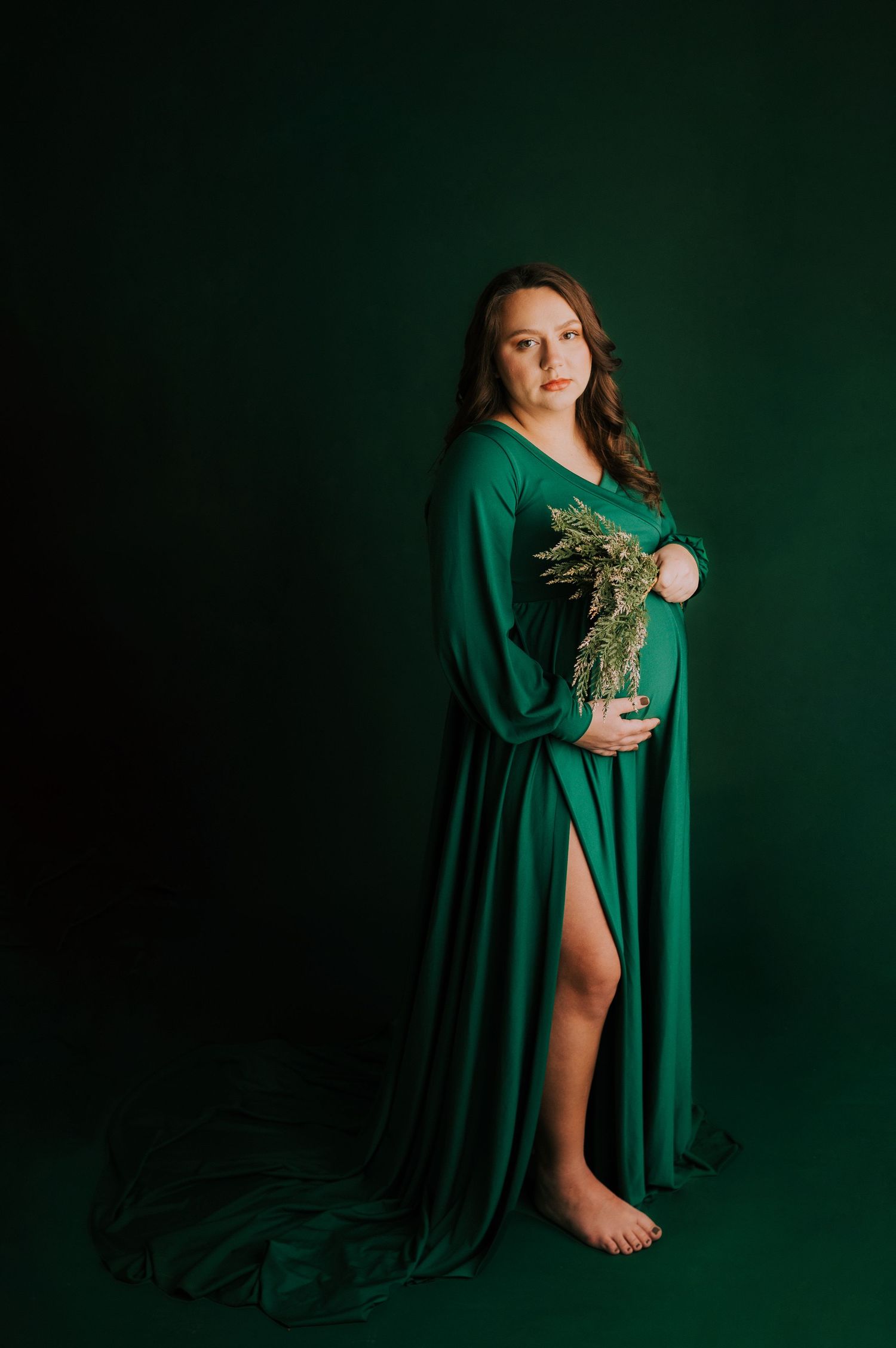 Dramatic portraits in emerald green dress against dark background with moody lighting.