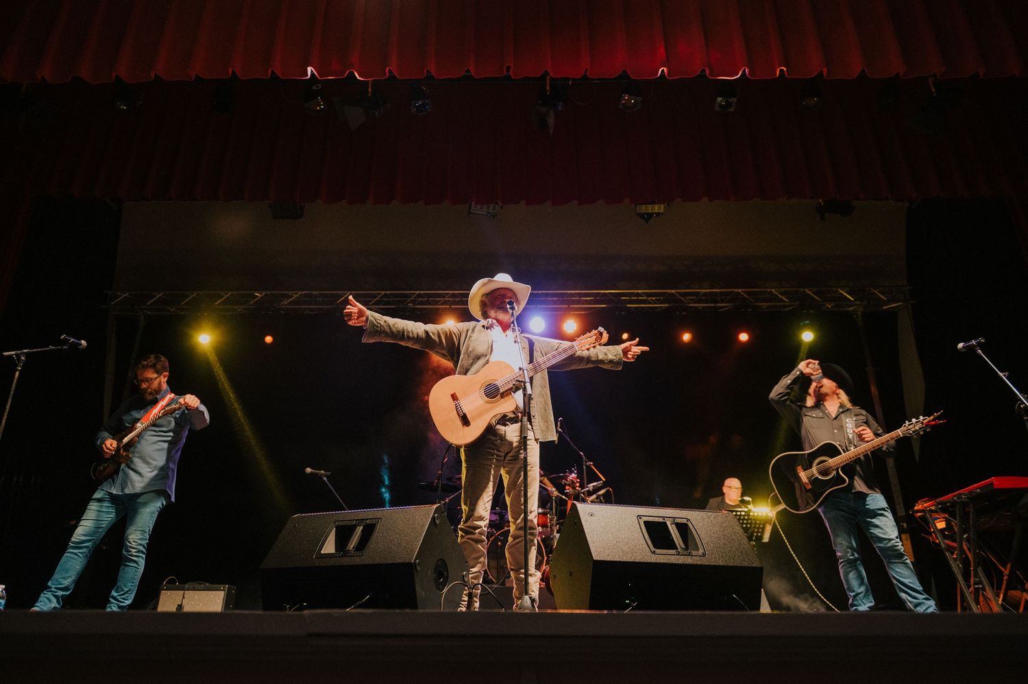 Musicians perform on stage with acoustic guitars under dramatic red lighting during a live concert performance.