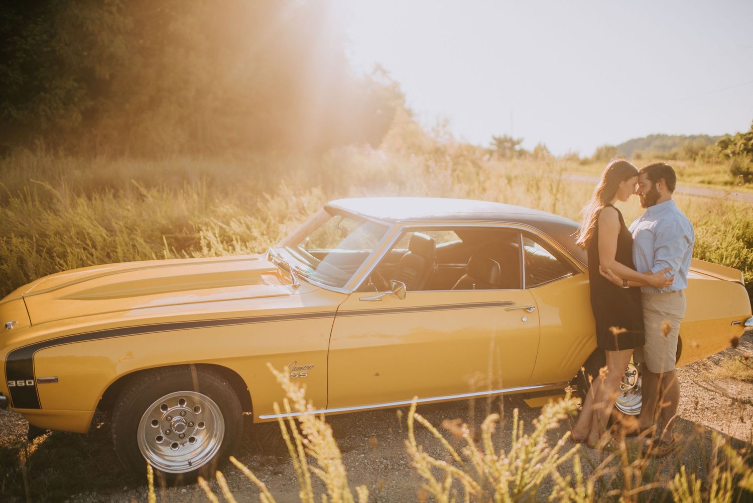 A vintage gold-colored car photographed at sunset with a romantic couple silhouette.