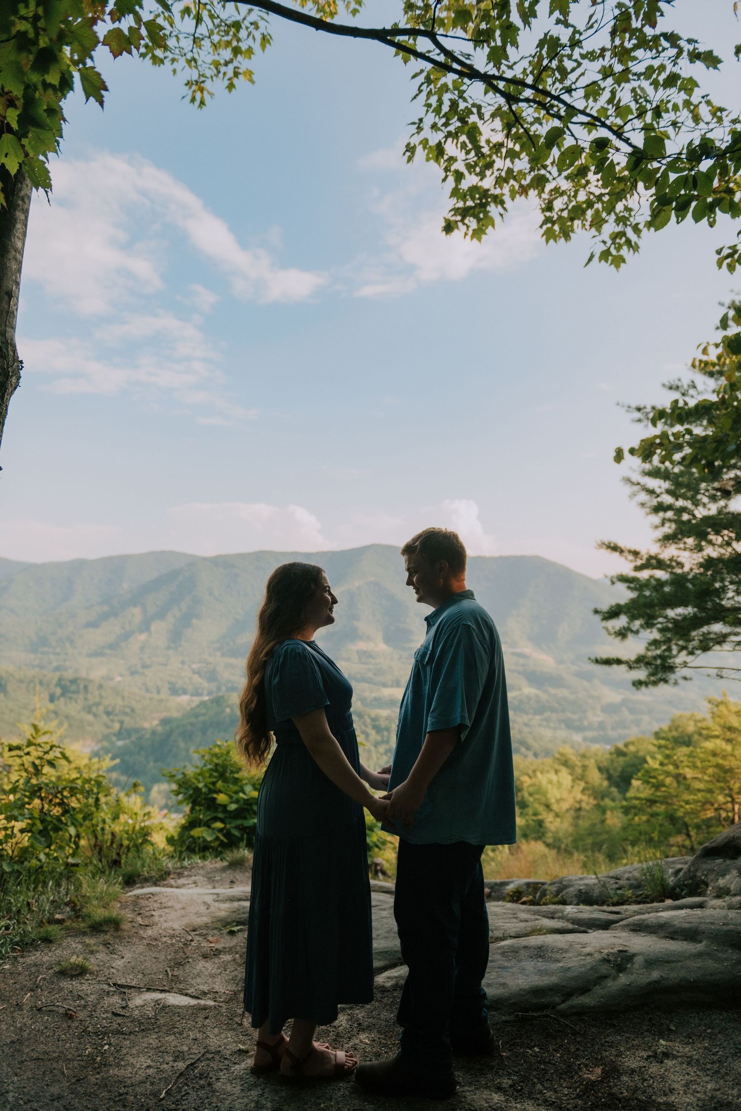 A couple shares a romantic moment while overlooking scenic mountain views on a sunny day.