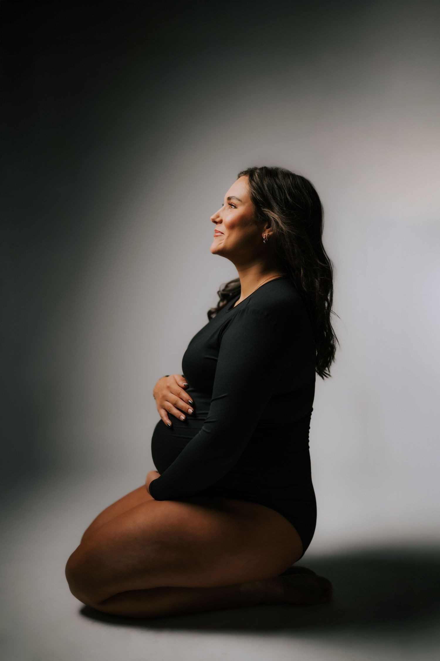 A silhouetted figure in a black outfit sits in artistic poses against a minimalist gray backdrop in a photo series.