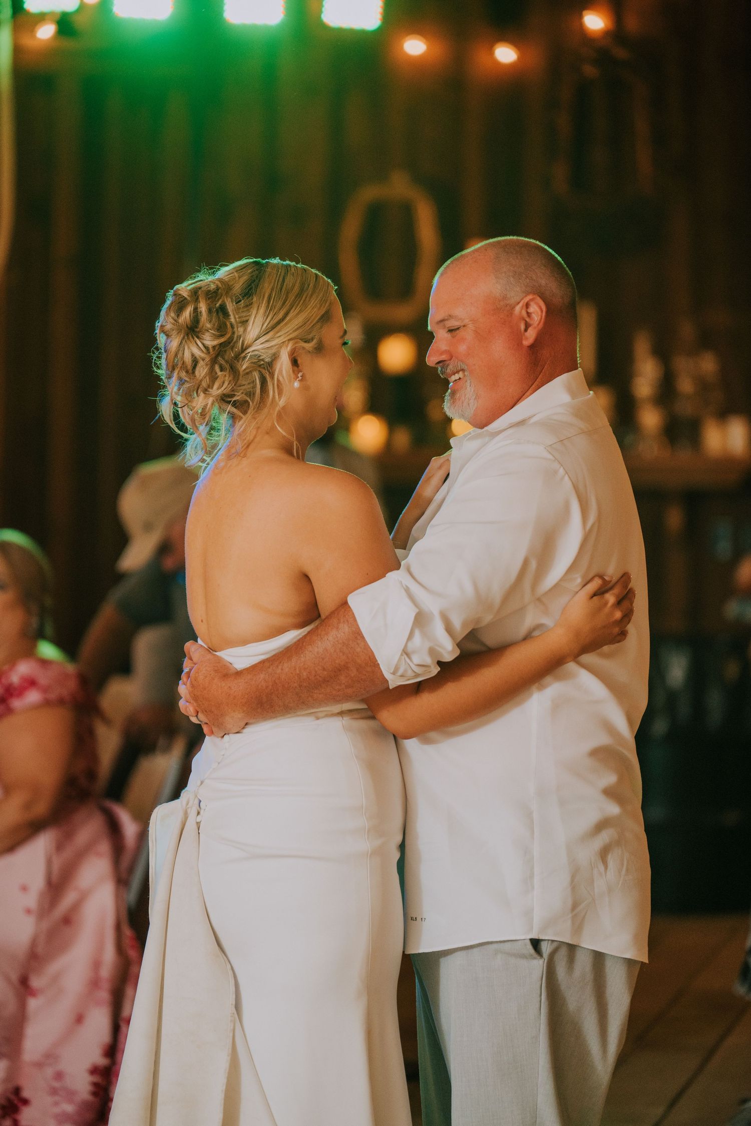 A couple shares their first dance at their wedding reception under colorful lighting.